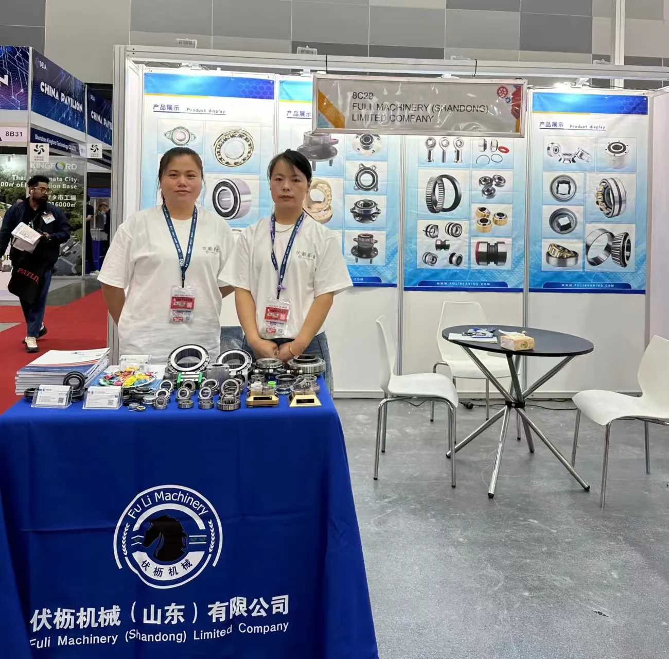 Two FULI staff at a trade fair booth with samples on the table and a Fuli Machinery (Shandong) Limited Company banner behind them