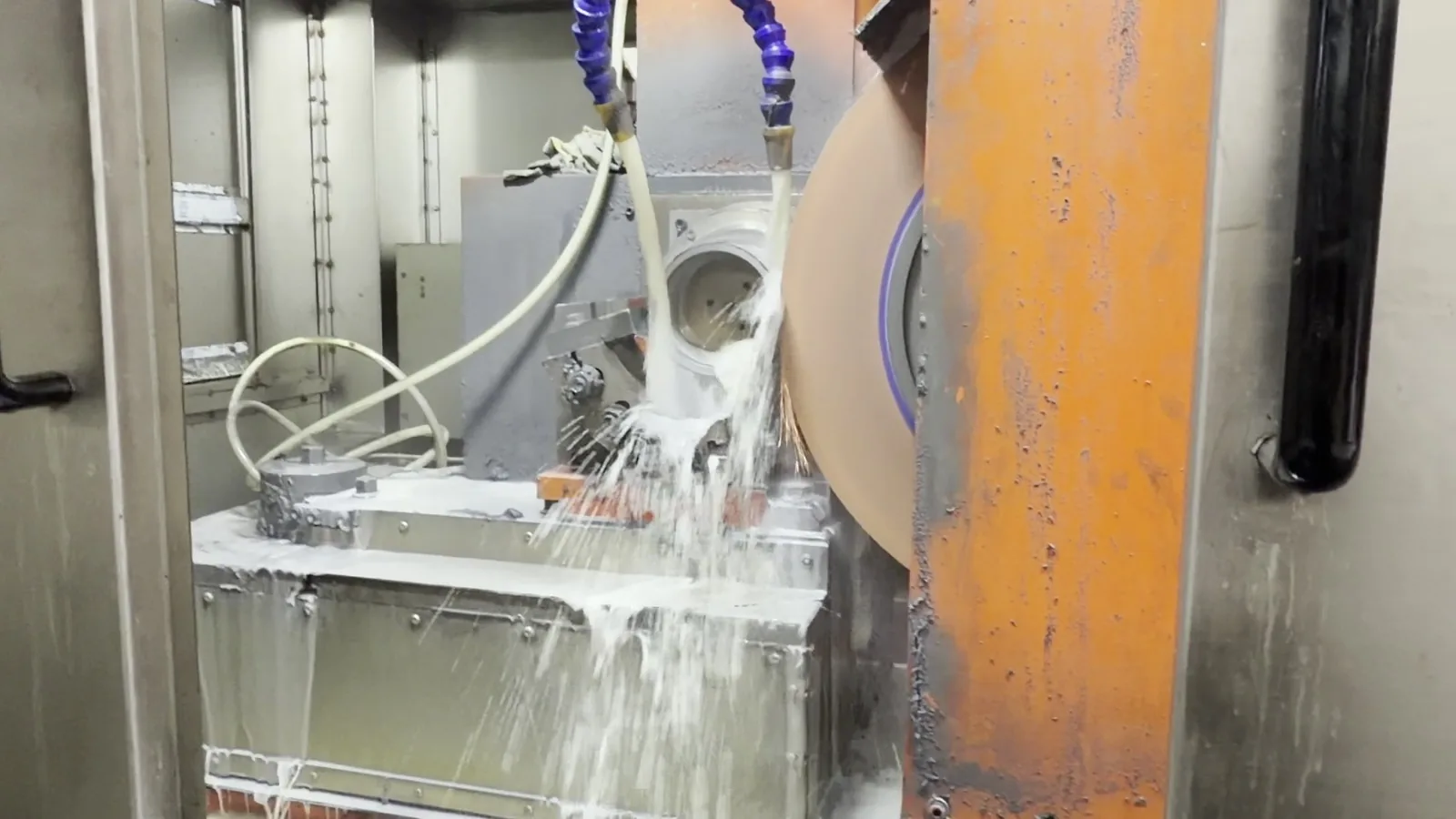 A grinding wheel working a steel ring blank under a spray of coolant
