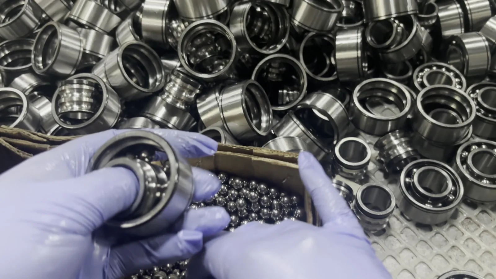 Gloved hands fitting steel balls into a ball bearing above a bin of bearings