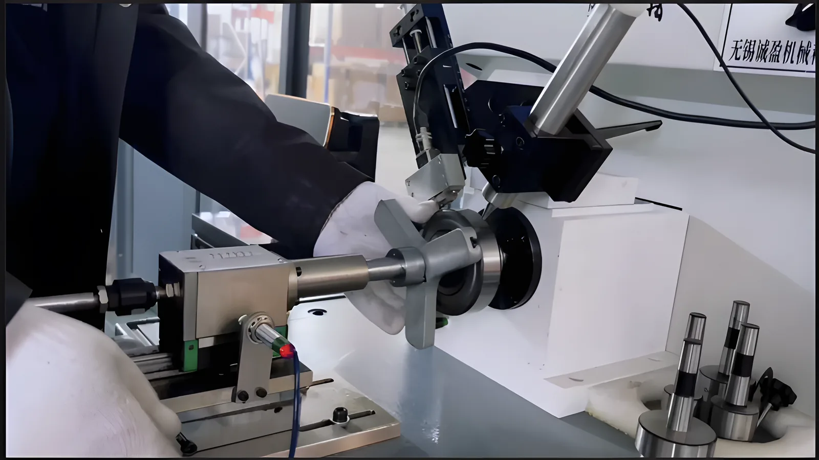 A gloved hand holding a bearing on a vibration and noise tester, with the sensor arm touching the outer ring